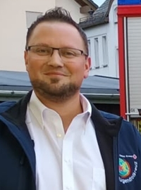 Christian Schilling, porträtiert in Hemd und Jacke mit Logo auf der Brust